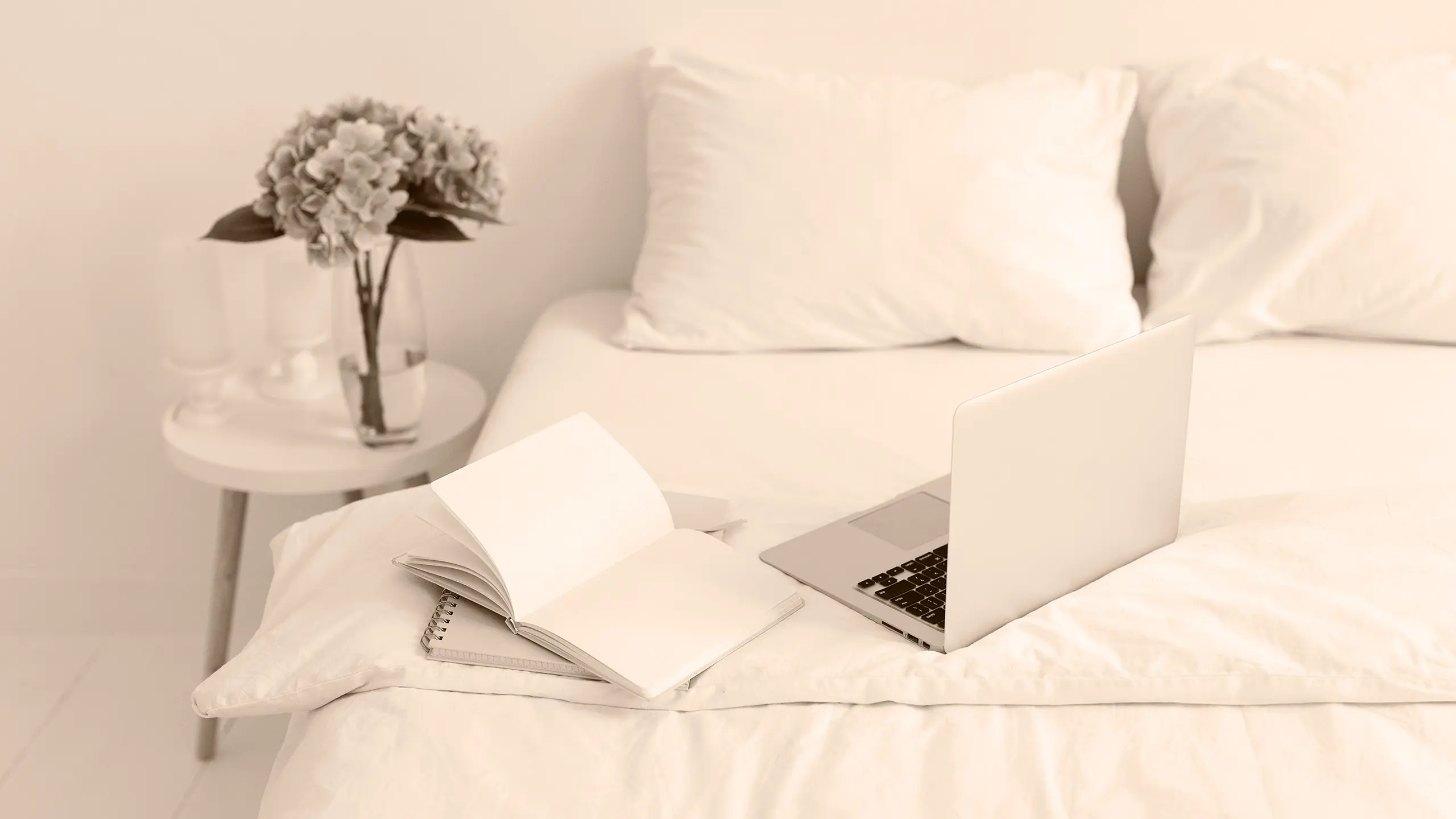 A laptop on a bed next to an open notebook.